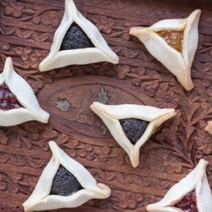 closeup of low FODMAP gluten-free Hamantaschen on wooden tray with poppy seed, strawberry and orange marmalade fillings