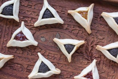 closeup of low FODMAP gluten-free Hamantaschen on wooden tray with poppy seed, strawberry and orange marmalade fillings