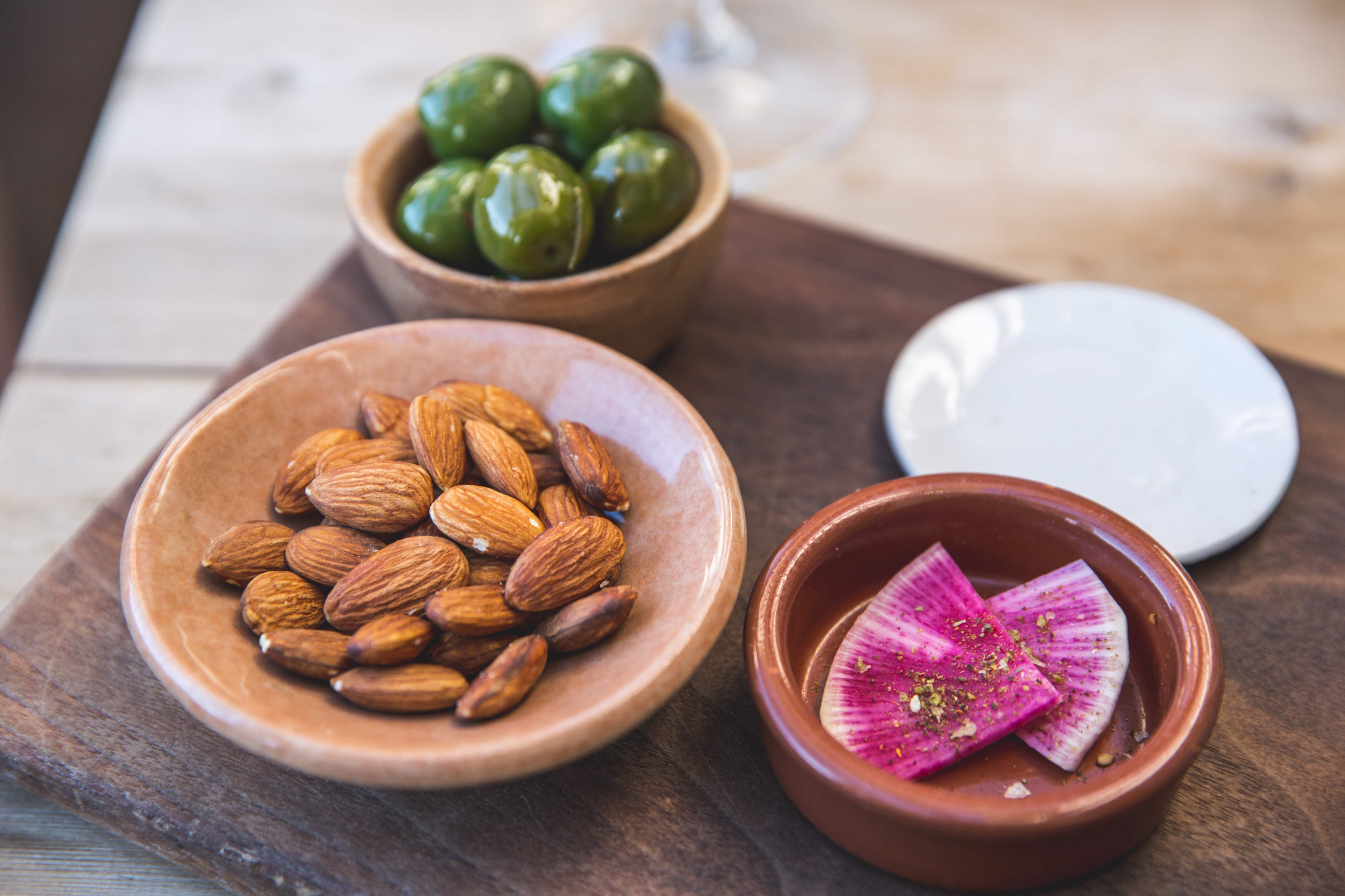  almonds, olives and radish in small ceramic dishes as a low FODMAP snack