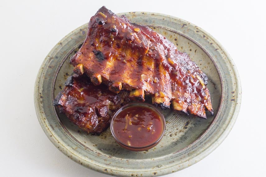 Oven-Roasted Orange Marmalade BBQ Ribs on rustic plate with small glass dish of extra sauce