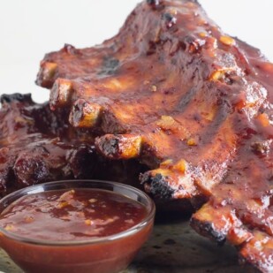 Low FODMAP Oven-Roasted Orange Marmalade BBQ Ribs on rustic plate with small glass dish of extra sauce
