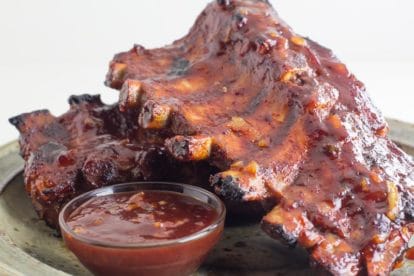 Low FODMAP Oven-Roasted Orange Marmalade BBQ Ribs on rustic plate with small glass dish of extra sauce