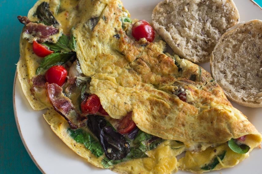 closeup of low FODMAP BLT omelet with blue cheese on a white plate; aqua wooden backdrop