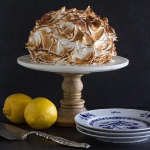 horizontal Low FODMAP lemon meringue cake on white pedestal with dark background