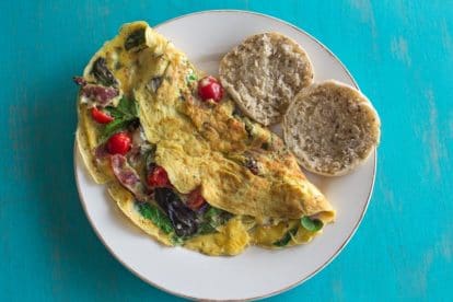 low FODMAP BLT omelet with blue cheese and gluten free English muffins on white plate against aqua background