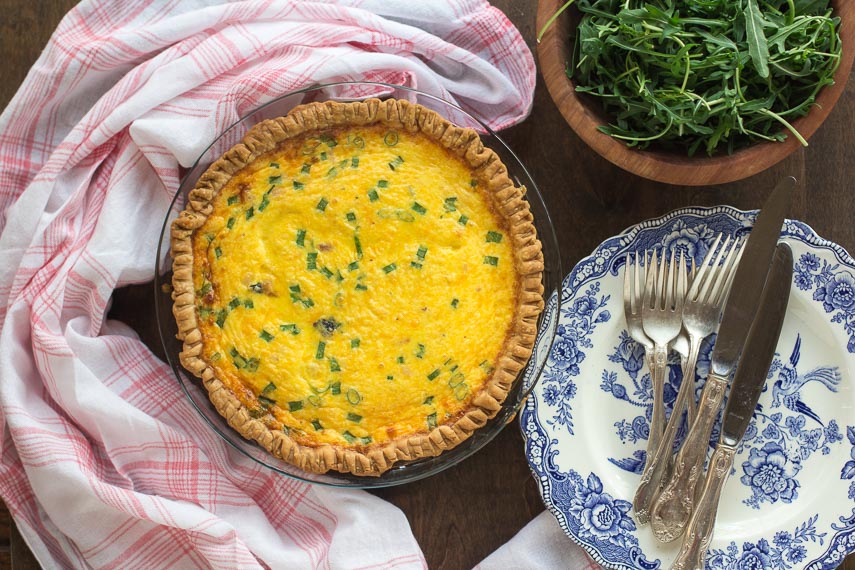 overhead image of ham & cheese low FODMAP quiche, whole, in pie pan with blue and white plates alongside