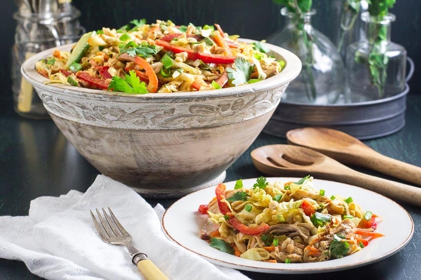 Low FODMAP Asian Chicken Salad in wooden bowl and also on a white plate; wooden serving spoons in background