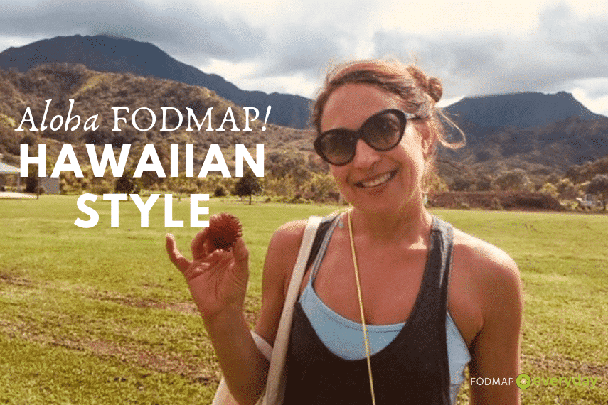 A young woman holding a small fruit while standing in front of a Hawaiian mountain.