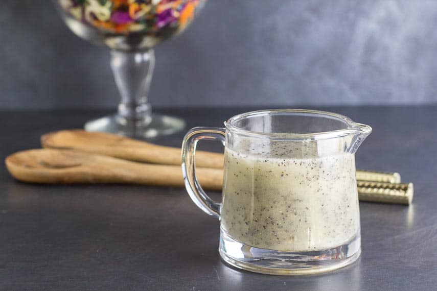 low FODMAP poppy seed dressing in a clear glass pitcher with wooden serving implements in background