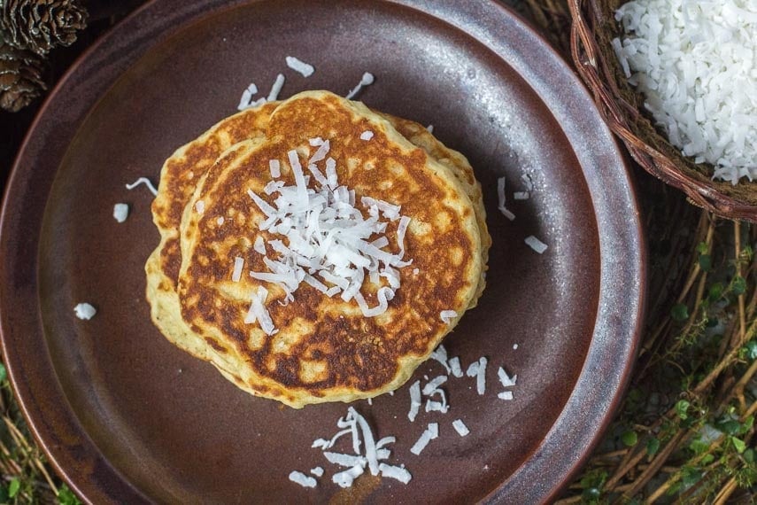 overhead image of Low FODMAP Browned-Butter Coconut Pancakes on a brown dish, with coconut in a dish alongside