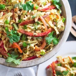 overhead view of Low FODMAP Asian Chicken Salad in wooden bowl; plate and wooden serving implements in background