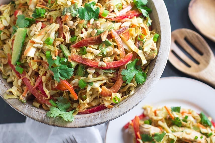 overhead view of Low FODMAP Asian Chicken Salad in wooden bowl; plate and wooden serving implements in background