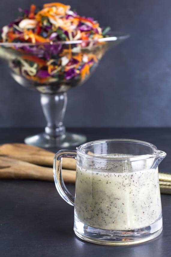 vertical image of low FODMAP Poppy Seed Dressing in clear pitcher against a dark background