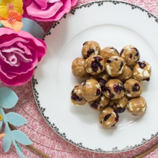 Low FODMAP Cranberry White Chocolate Energy Balls on white plate with fabric flower alongside; pink placemat in background