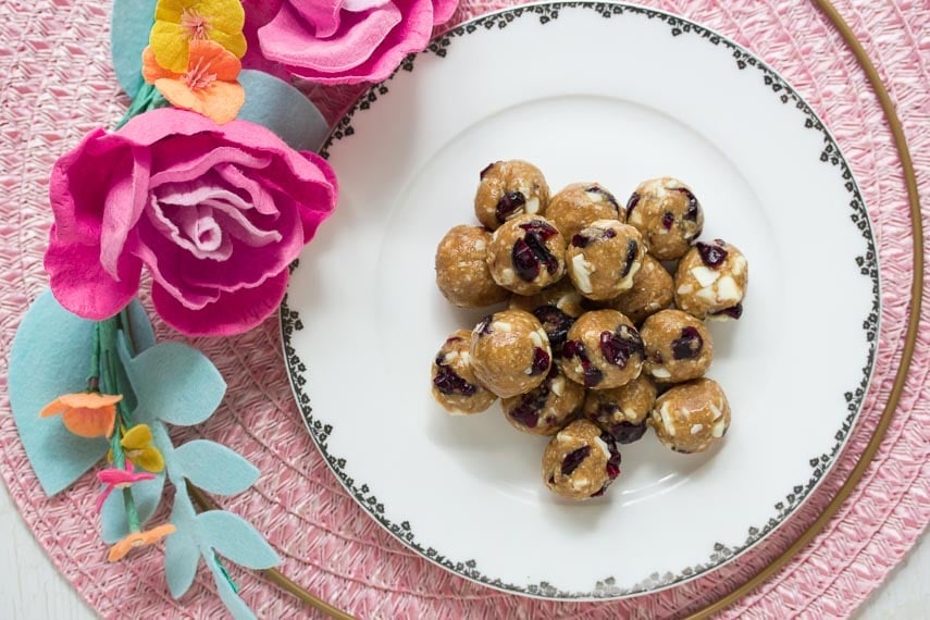 Low FODMAP Cranberry White Chocolate Energy Balls on white plate with fabric flower alongside; pink placemat in background