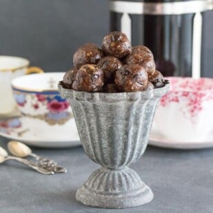 Low FODMAP Mocha Espresso Power Balls in a grey aluminum footed dish; coffee cups, French press coffee pot and spoons in background