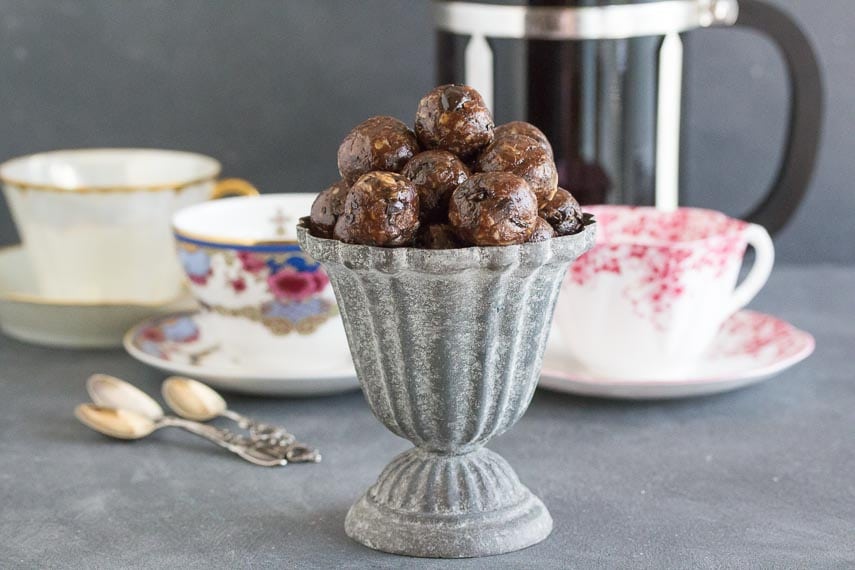 Low FODMAP Mocha Espresso Power Balls in a grey aluminum footed dish; coffee cups, French press coffee pot and spoons in background