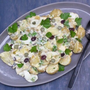 Low FODMAP Tangy Potato & Egg Salad with Olives & Pickles on a grey oval platter against a blue backdrop