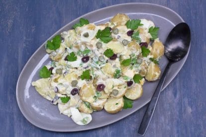 Low FODMAP Tangy Potato & Egg Salad with Olives & Pickles on a grey oval platter against a blue backdrop