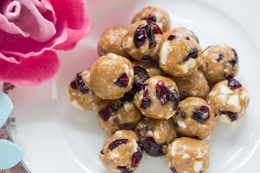Pile of Low FODMAP Cranberry White Chocolate Energy Balls on white plate with fabric flower alongside