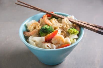 aqua bowl of low FODMAP shrimp and broccoli with noodles; chopsticks on top of bowl edge