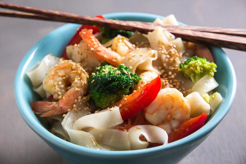 aqua bowl of low FODMAP shrimp and broccoli with noodles; chopsticks on top of edge of bowl