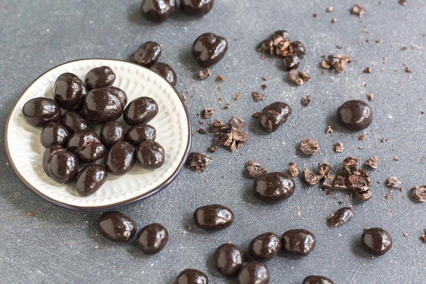 chocolate covered espresso beans in a small white dish and on a dark surface