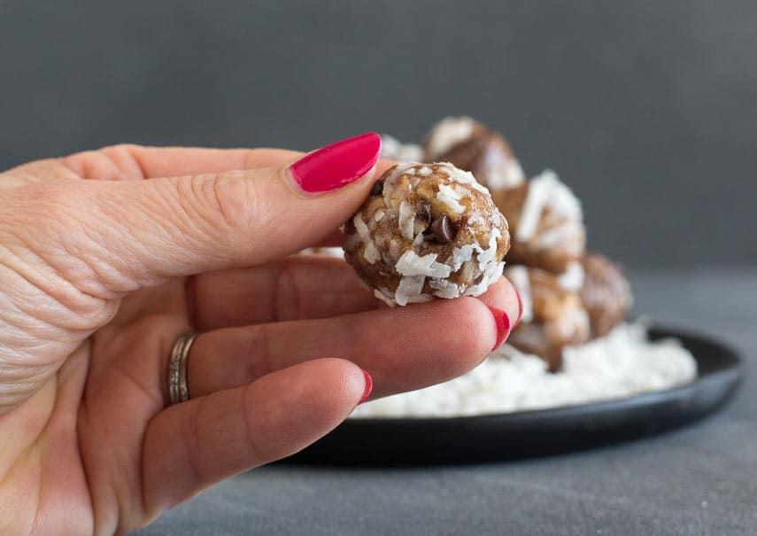 closeup of Low FODMAP Almond Joy Energy Bites in hand against dark background