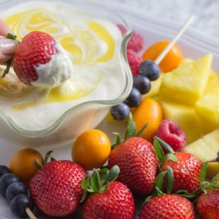 Low FODMAP Lime cheesecake dip in a decorative clear glass bowl; fruit alongside for dipping