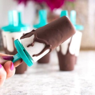 manicured hand holding a Low FODMAP Chocolate Covered Banana Popsicle_