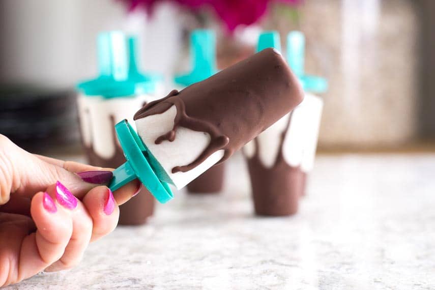 manicured hand holding a Low FODMAP Chocolate Covered Banana Popsicle_