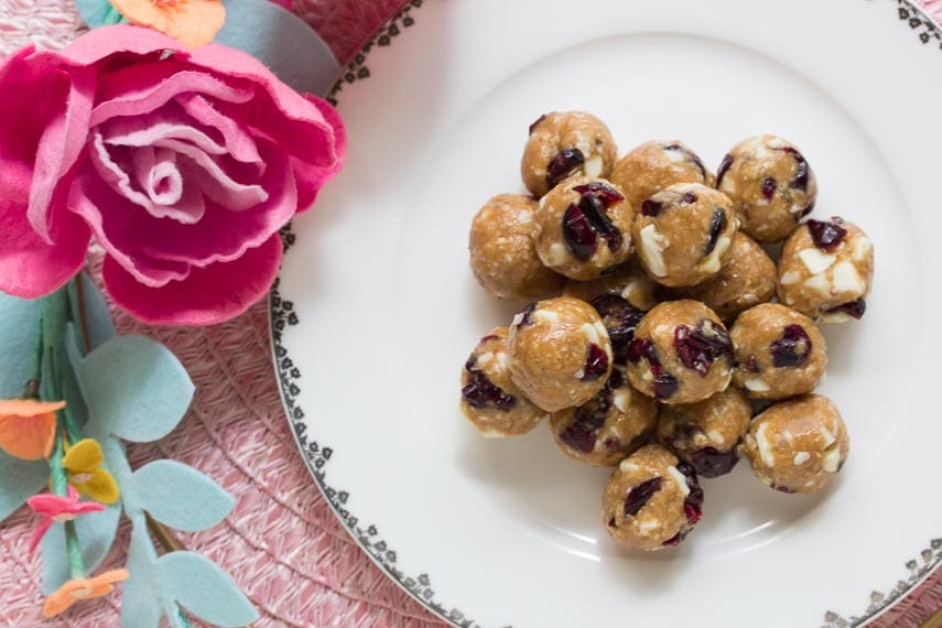 overhead image of Pile of Low FODMAP Cranberry White Chocolate Energy Balls on white plate with fabric flower alongside; pink placemat in background