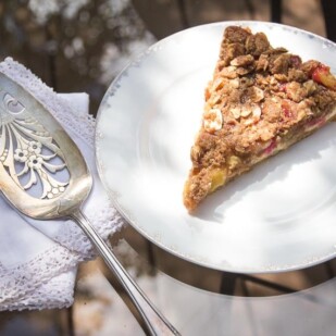 overhead shot of slice of Low FODMAP Rhubarb Cheesecake Tart on white plate, oustide on glass table_