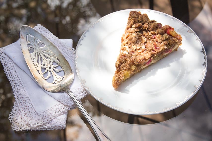 overhead shot of slice of Low FODMAP Rhubarb Cheesecake Tart on white plate, oustide on glass table_