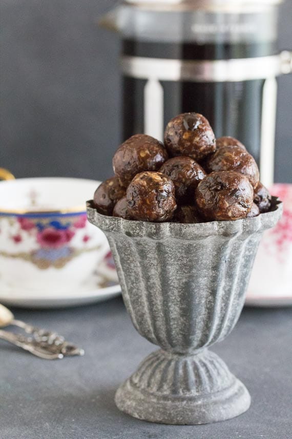 vertical image of Low FODMAP Mocha Espresso Power Balls in a grey aluminum footed dish; coffee cups and spoons in background