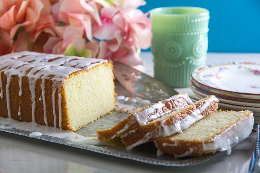 Glazed Low FODMAP Lemon Loaf on tin tray with plates in background