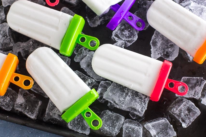 Low FODMAP Coconut Popsicles on a dark tray filled with ice