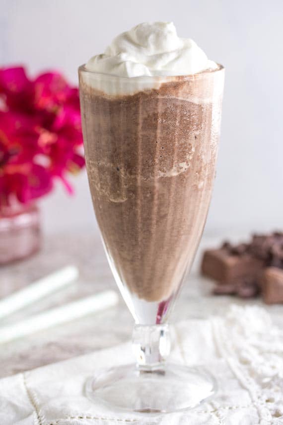 Low Frozen Hot Chocolate in glass goblet with whipped cream on top on white lacy doily