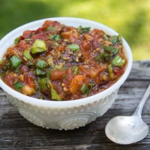 White bowl containing grilled tomato and peach salsa with spoon alongside