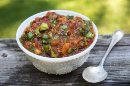 White bowl containing grilled tomato and peach salsa with spoon alongside