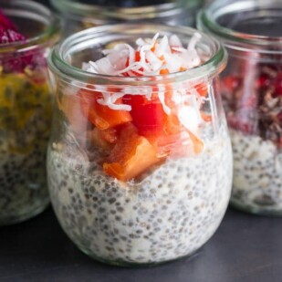 glass jar of overnight oats and chia topped with papaya and coconut against dark background