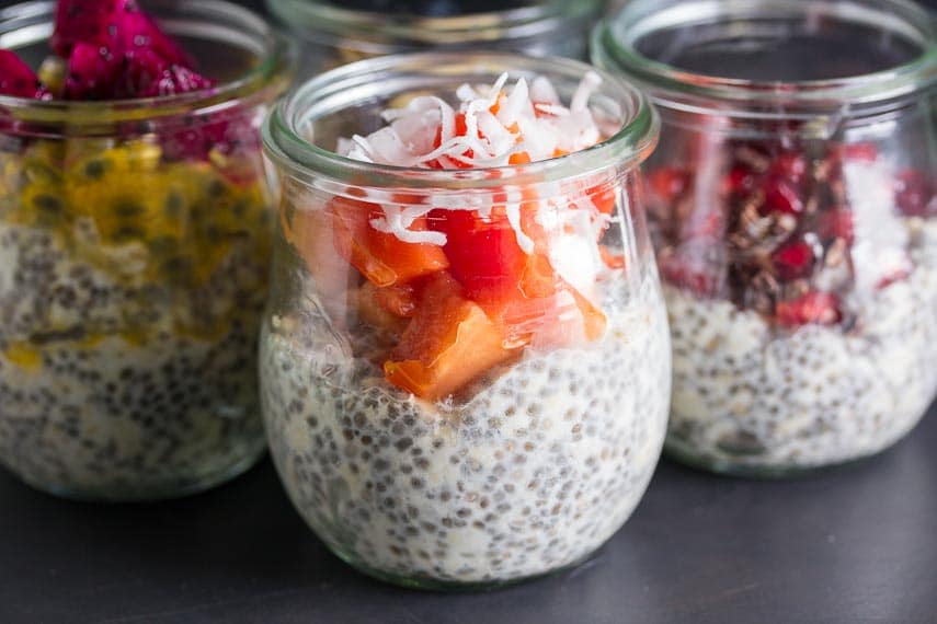 glass jar of overnight oats and chia topped with papaya and coconut against dark background