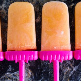 icy low FODMAP Cantaloupe lime popsicles on dark quartz surface