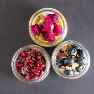 overhead shot of a trio of overnight oats and chia in glass bowls topped with colorful fruit