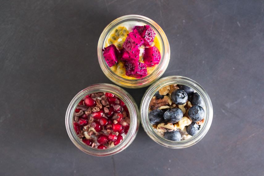 overhead shot of a trio of overnight oats and chia in glass bowls topped with colorful fruit