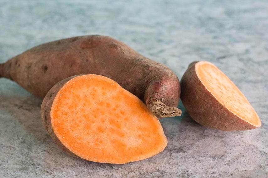 sweet potato, whole and cut open, on grey quartz surface