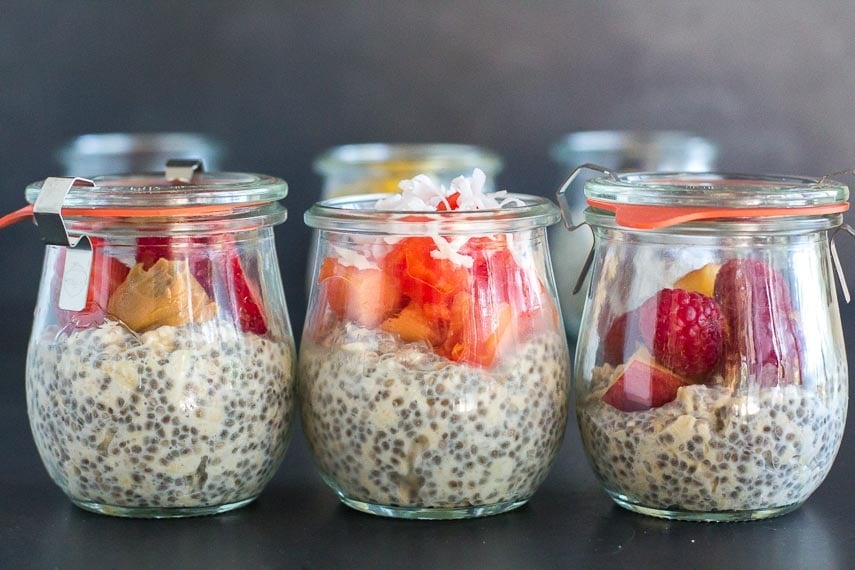 trio of glass jars holding overnight oats and chia with fruit against dark background