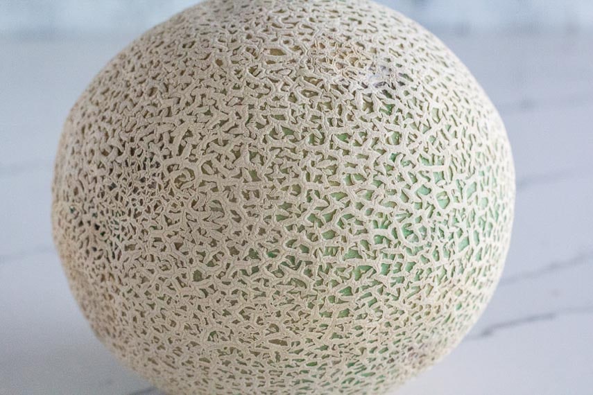unripe cantaloupe showing green skin against marble surface