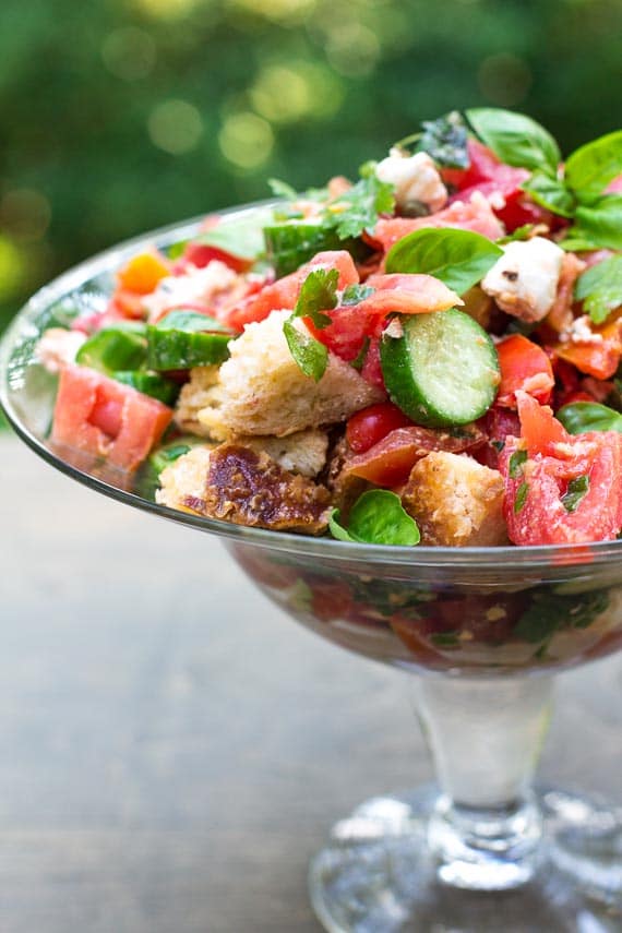 vertical low FODMAP Panzanella with Tomatoes, Cucumbers & Basil in glass pedestal dish on the deck