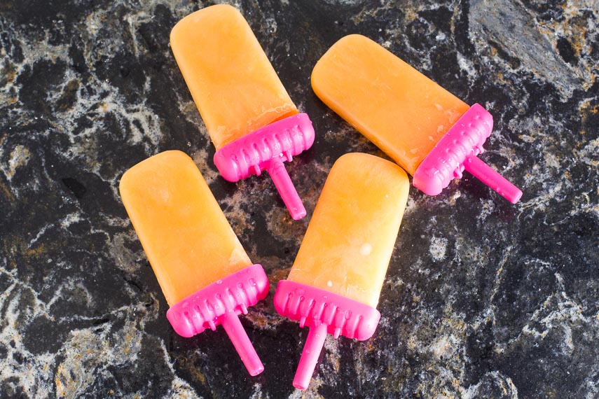 Cantaloupe Lime Popsicles in pink plastic holders against dark quartz surface